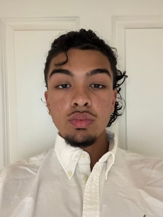 Portrait of a person with dark curly hair wearing a white button-up shirt, looking directly at camera against a light background