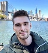 Man posing for selfie with Brooklyn Bridge and Manhattan skyline in background across the water